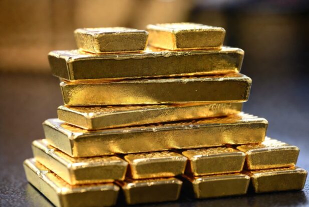 Pile of shiny gold bars stacked on a dark surface, forming a small pyramid.