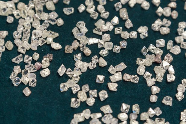 Many small translucent crystals scattered on a dark teal surface, resembling coarse salt or sugar crystals.